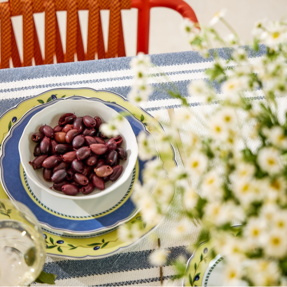 A white bowl containing dark olives on a blue-and-yellow patterned plate by Hutschenreuther, with a red chair and daisies in the background.