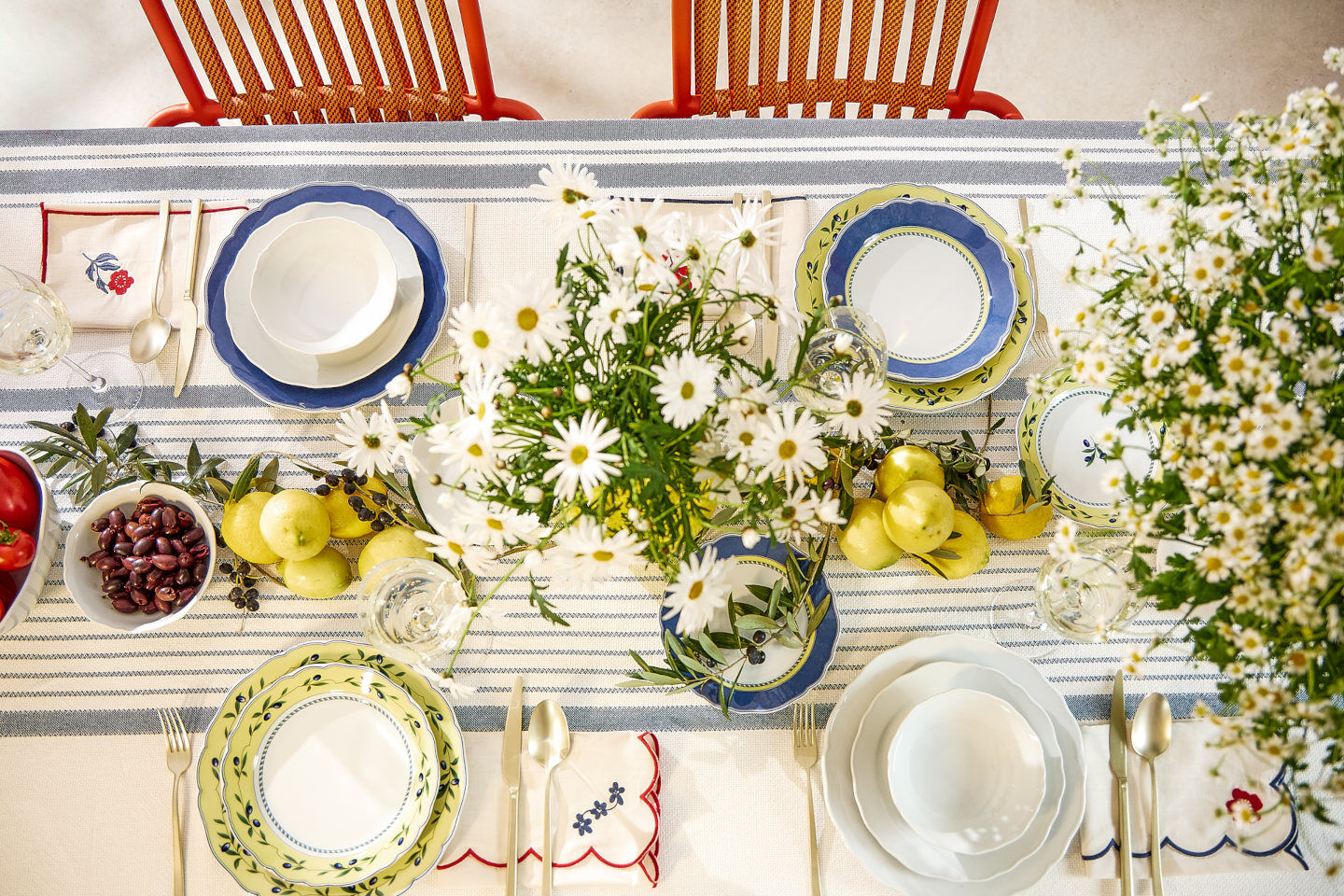 Ein bunt gedeckter Tisch mit blau-gelben und wei&szlig;em Geschirr uns Margeriten und Zitronen als zentrale Deko von oben fotografiert