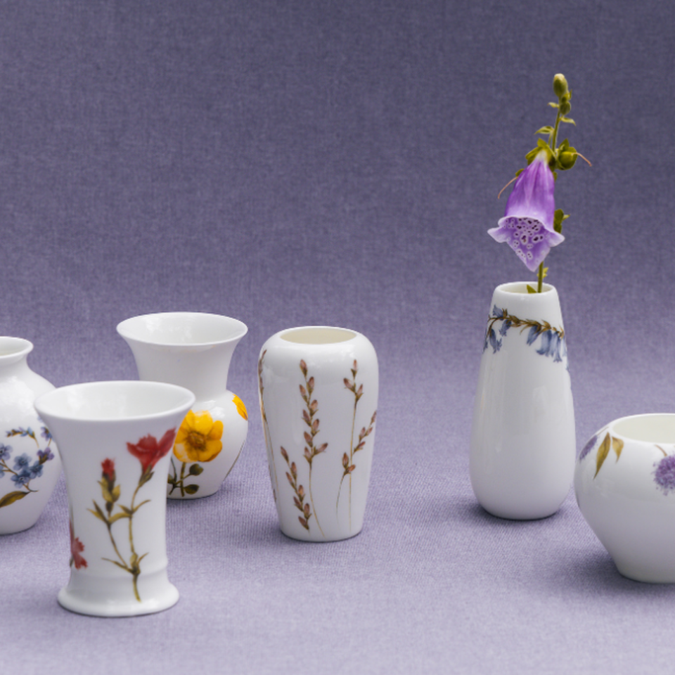 Piccoli vasi in porcellana Rosenthal con delicati motivi floreali su sfondo in tessuto viola – eleganza raffinata in serie.