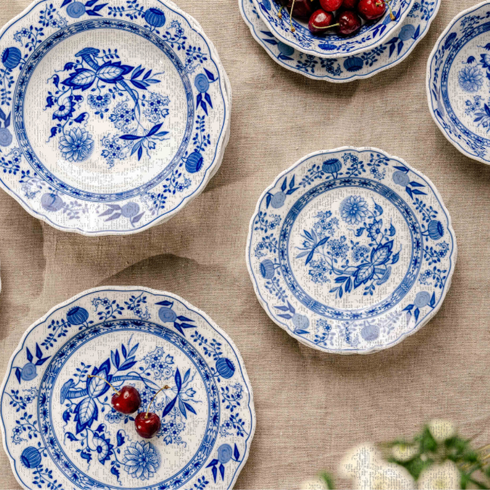 Servizio di piatti Hutschenreuther con decorazione blu a motivo cipolla disposto su un tovagliato di lino chiaro, decorato con piccole bacche rosse.