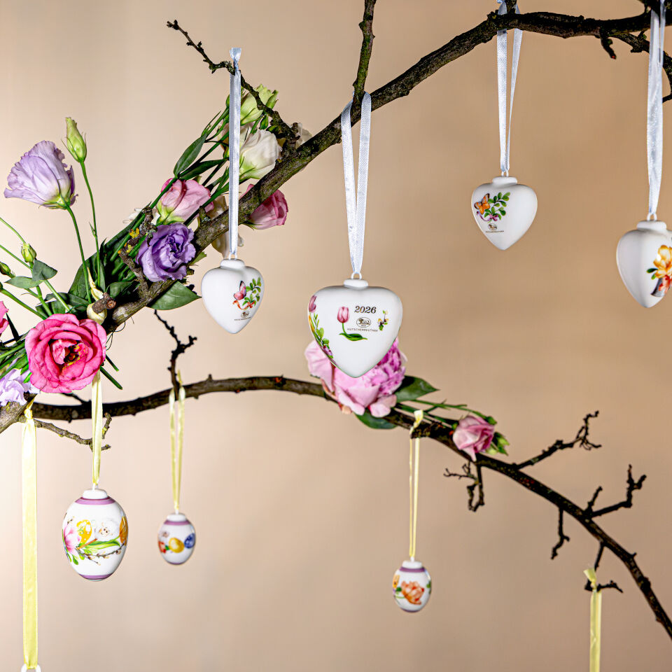 Cuori in porcellana Hutschenreuther 2026 con motivi floreali come decorazione pasquale su un ramo fiorito.