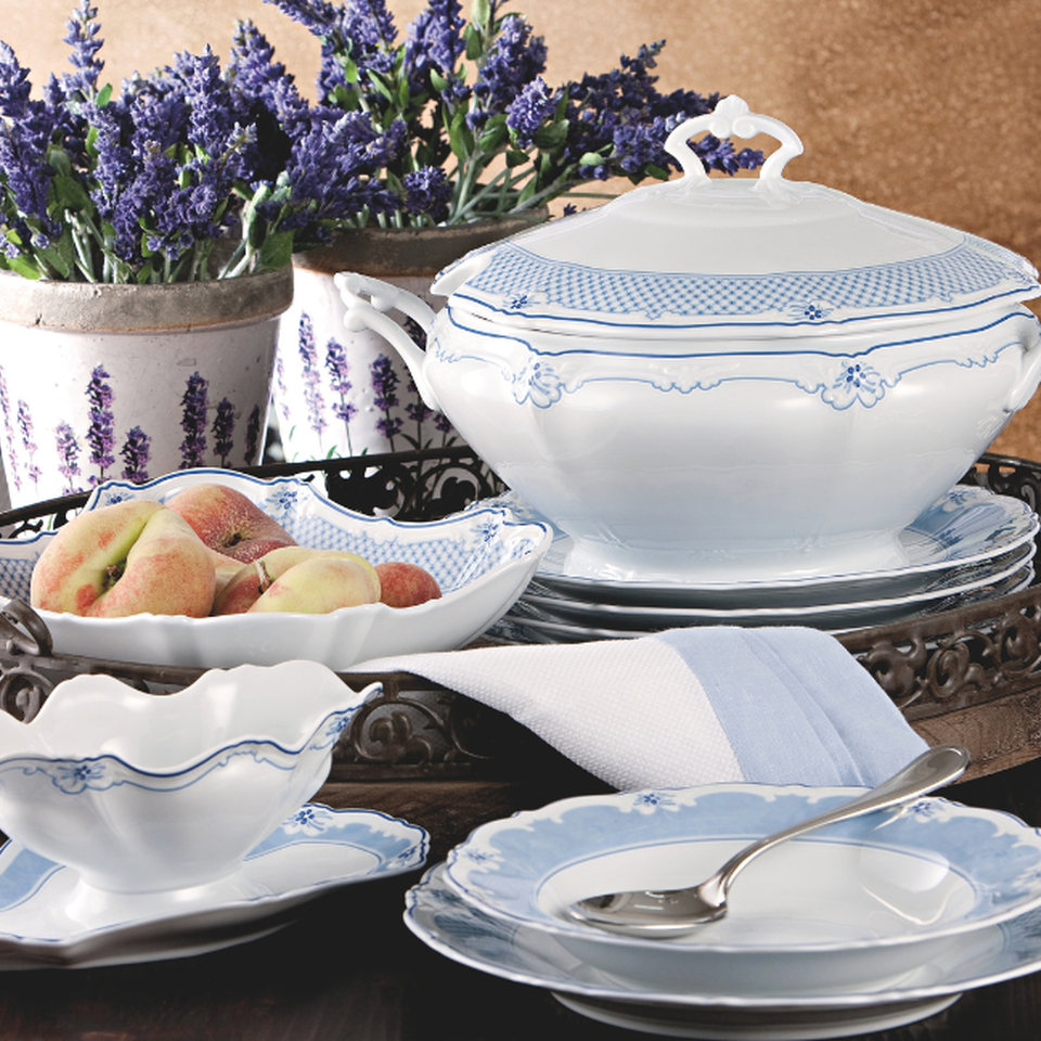 Elegante servizio di porcellana Hutschenreuther Baronesse in bianco e blu con decorazioni floreali, disposto su un vassoio con terrina, ciotole e lavanda sullo sfondo.