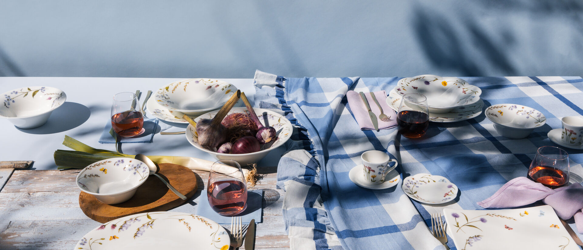 Stoviglie Hutschenreuther con motivi floreali su una tavola apparecchiata all'aperto, con piatti, ciotole e tazze dai colori pastello.