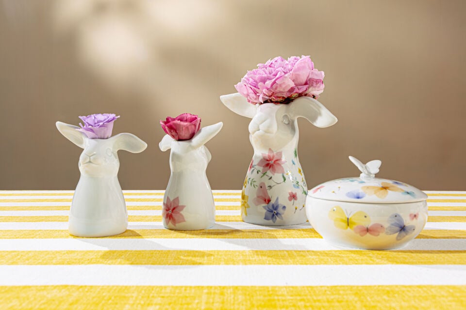 Drei Hasenvasen mit einer Blume auf einer gelb-wei&szlig; gestreiften Tischdecke