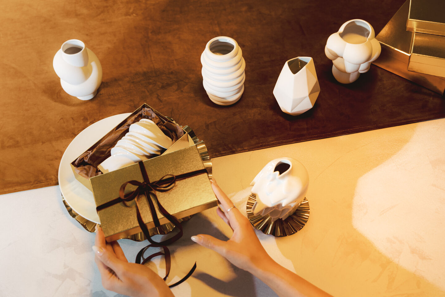 Goldenes Geschenk wird ausgepackt. Daneben stehen verschiedene wei&szlig;e Midi-Vasen von Rosenthal.