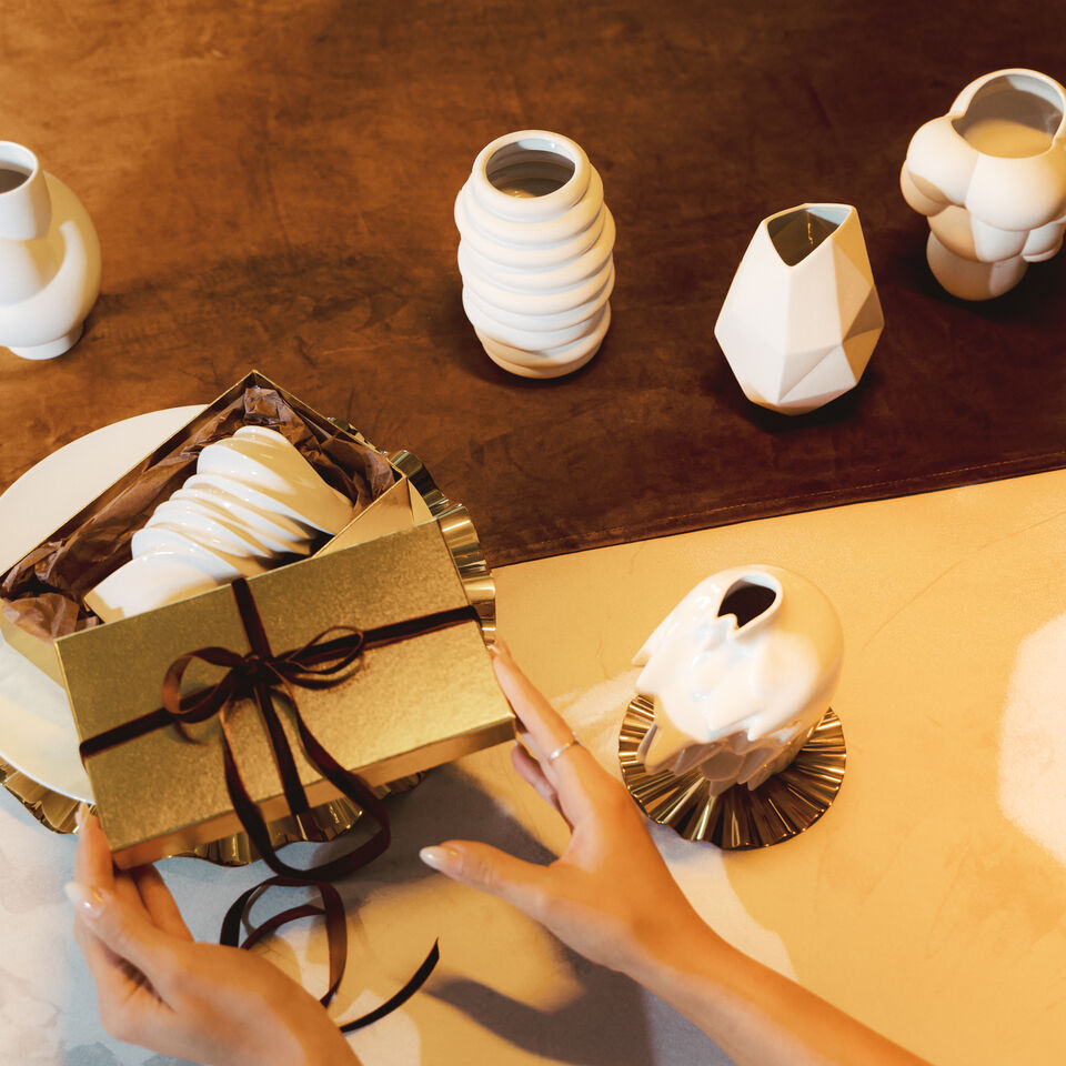Goldenes Geschenk wird ausgepackt. Daneben stehen verschiedene wei&szlig;e Midi-Vasen von Rosenthal.
