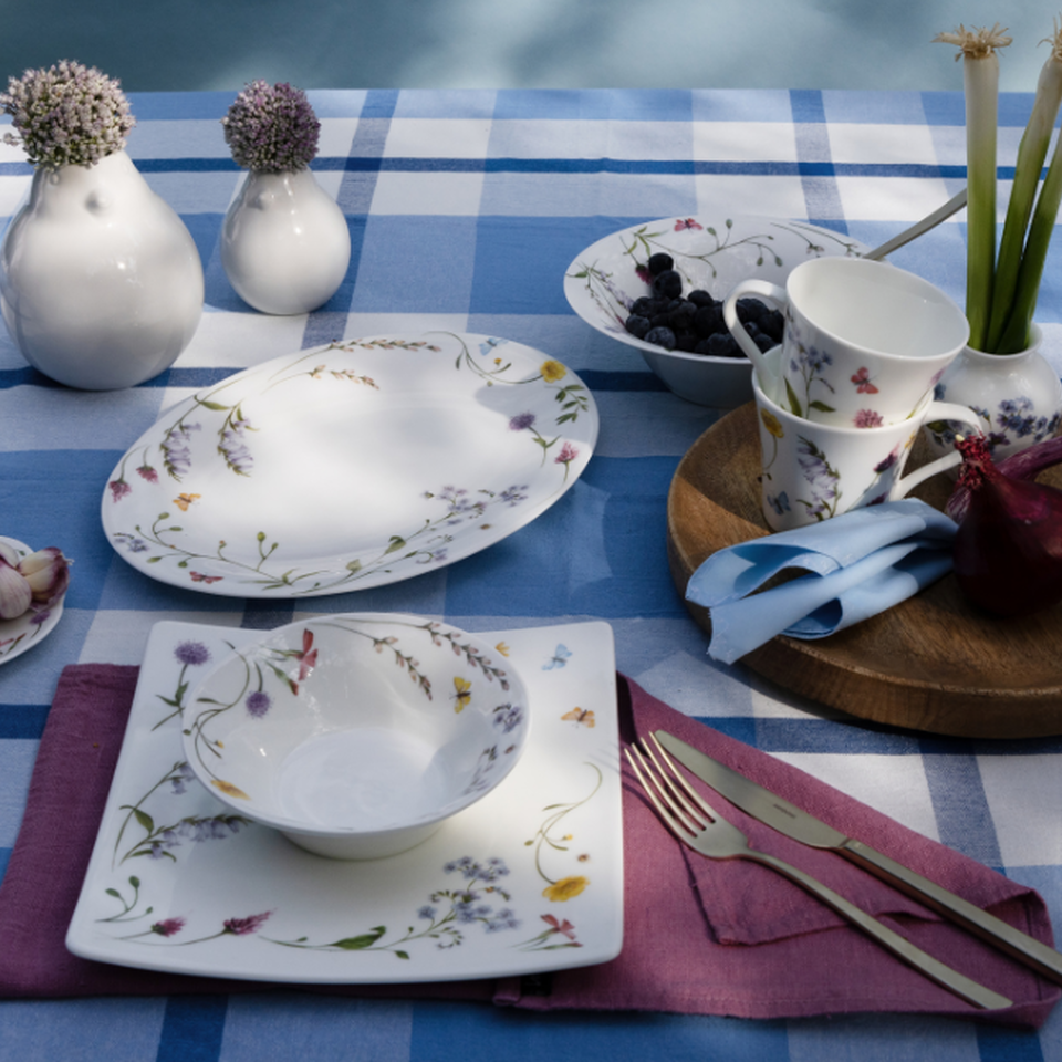 Servizio di piatti Hutschenreuther con delicati motivi floreali su tovaglia a quadretti blu e bianchi, abbinato a piatti, ciotole, tazze e decorazioni primaverili.