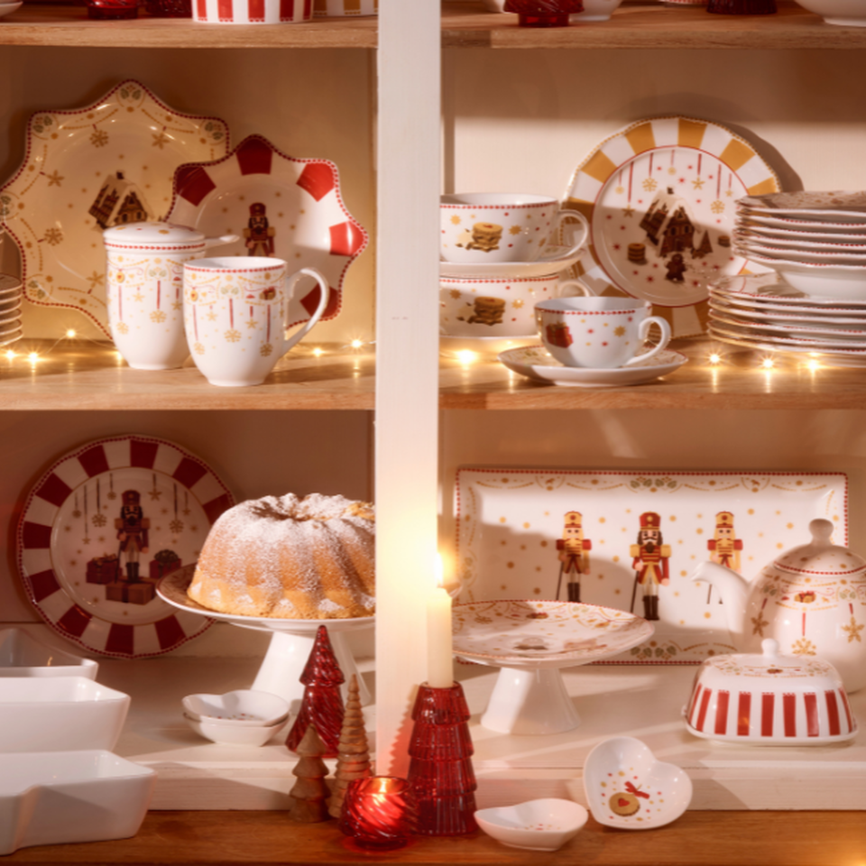 Credenza con porcellane natalizie: piatti, tazze e ciotole impilati con motivi festivi sugli scaffali.