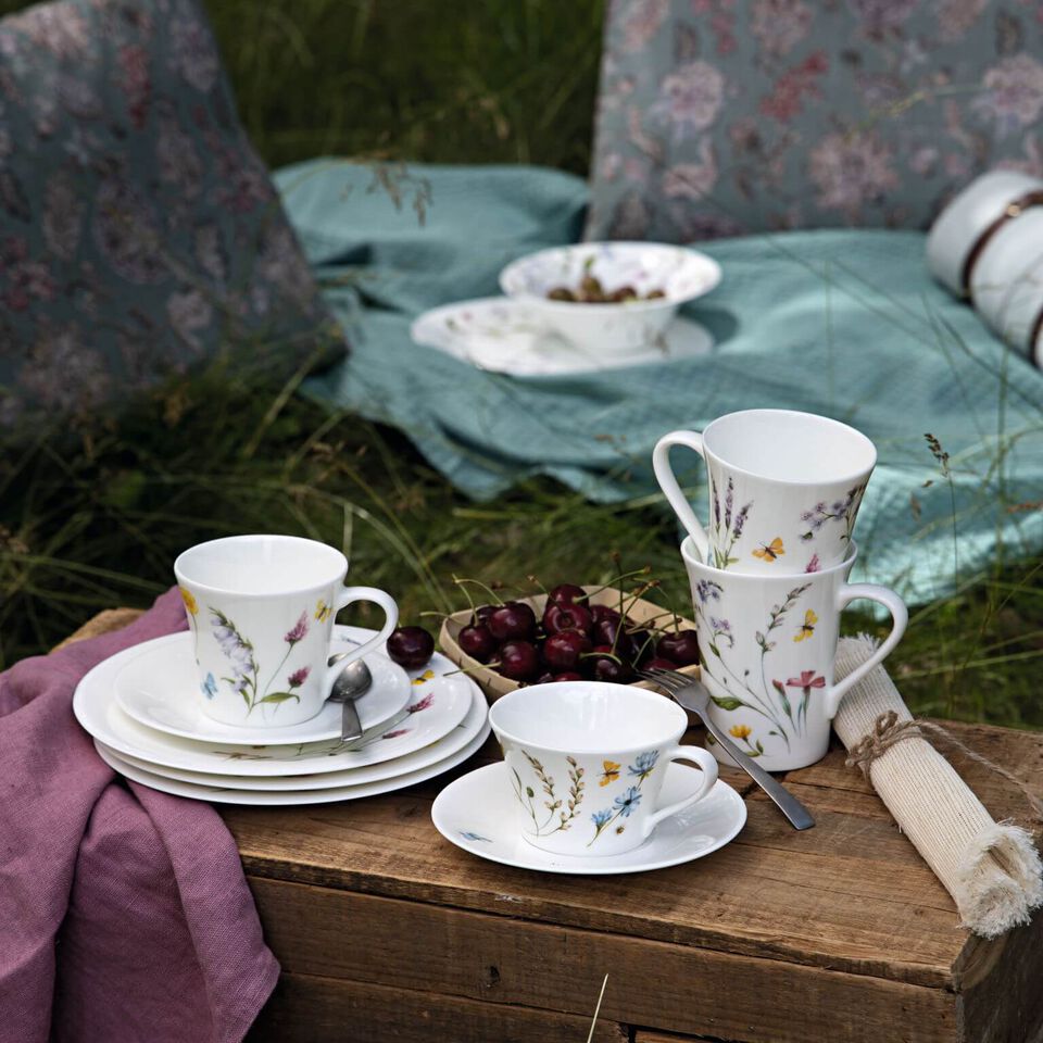 Porcellane Hutschenreuther con motivi floreali su una tavola rustica apparecchiata nel giardino primaverile.