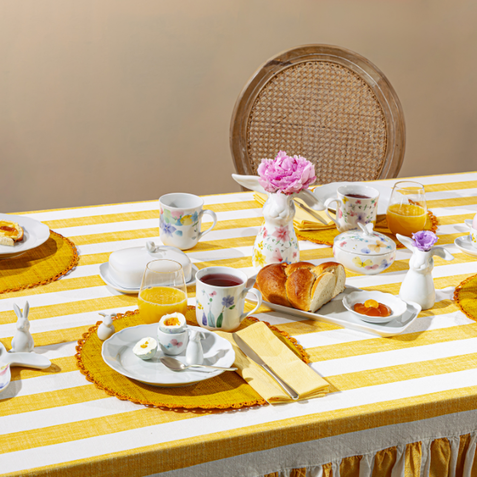 Tavola pasquale imbandita a festa con porcellane primaverili Hutschenreuther e decorazioni floreali nei toni del giallo e del rosa.