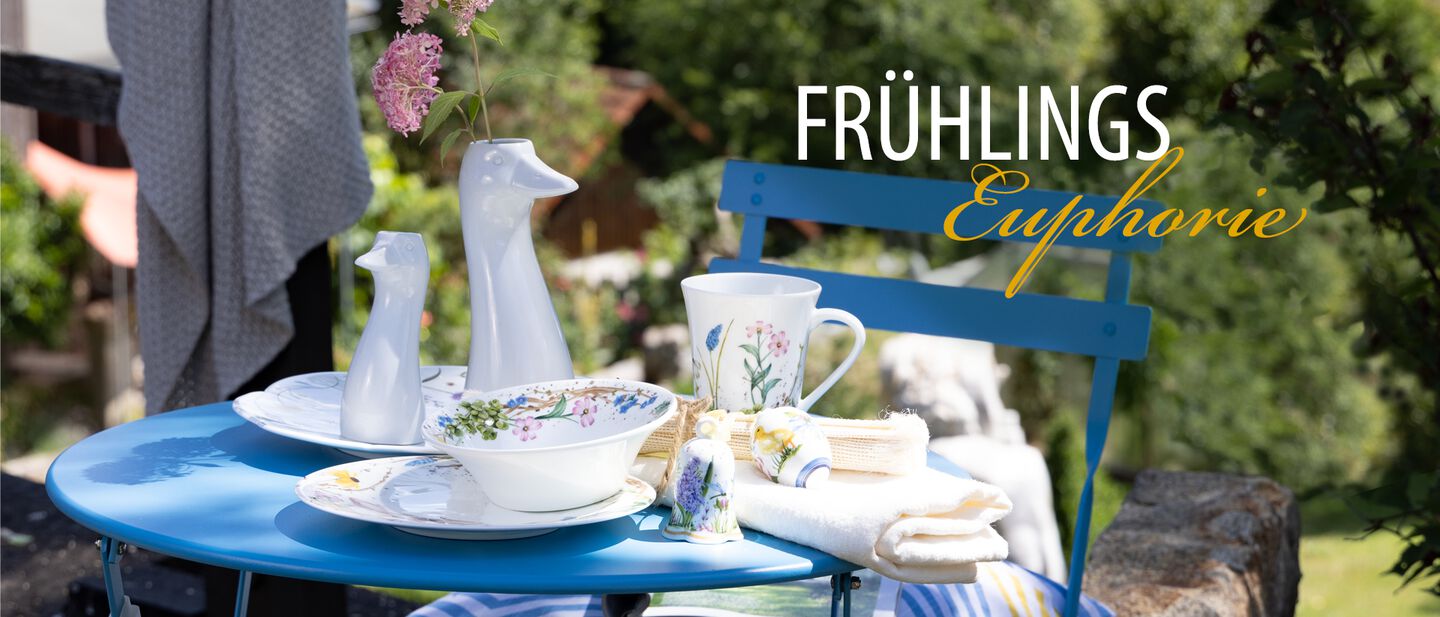 Hutschenreuther Frühlingsgeschirr und weiße Gans-Vasen auf blauem Gartentisch im Garten