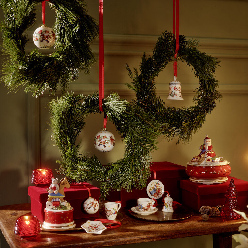 Christmas decorations hanging in wreaths made of fir branches, with various other Christmas decorations arranged on a table beneath them