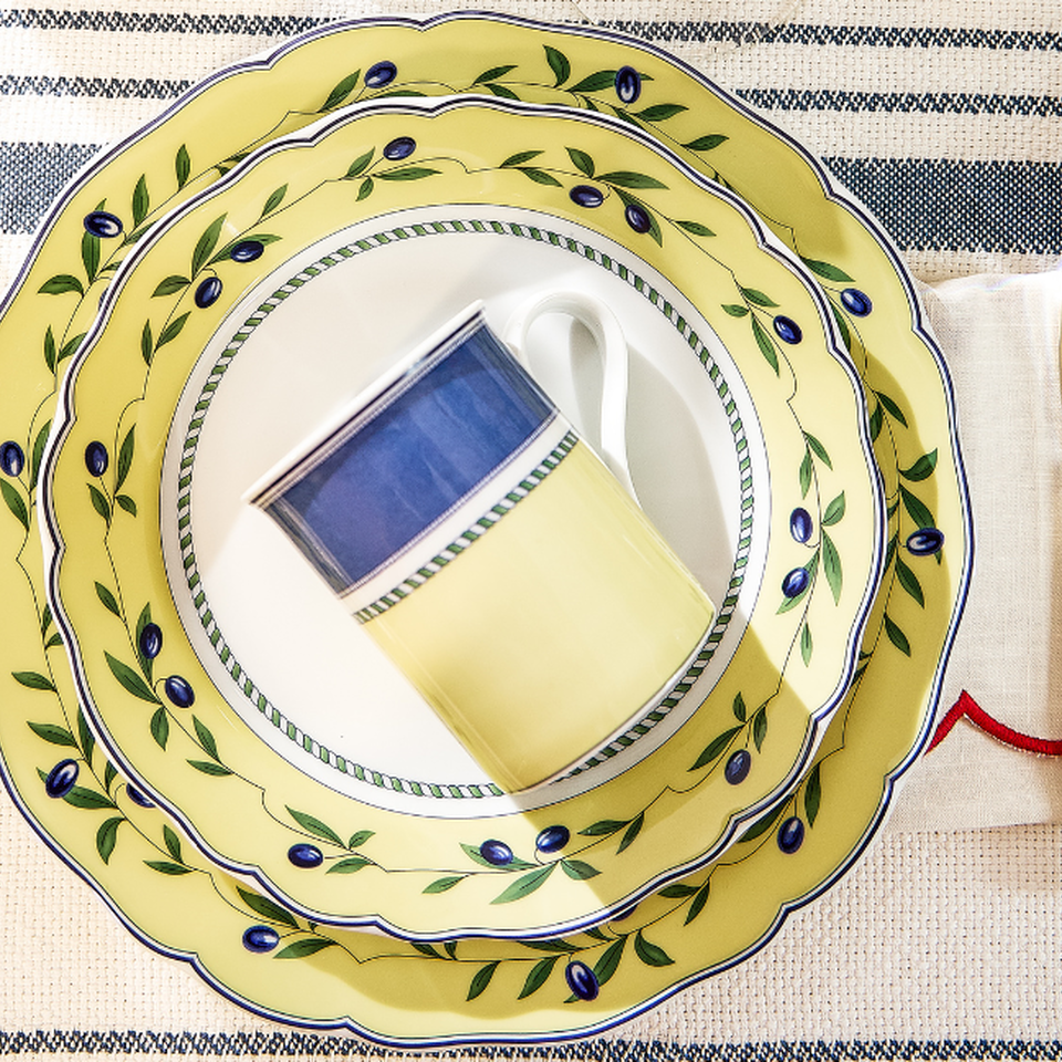 A place setting with a yellow and blue Hutschenreuther plate featuring an olive pattern and gold cutlery.