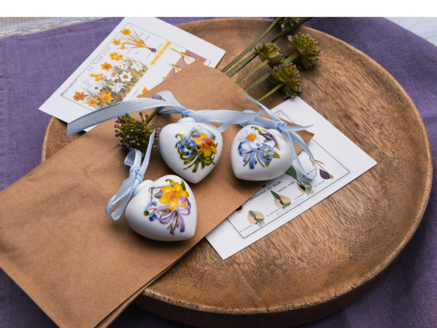 Three heart-shaped porcelain ornaments by Rosenthal with floral motifs and blue ribbons – beautifully arranged on kraft paper.