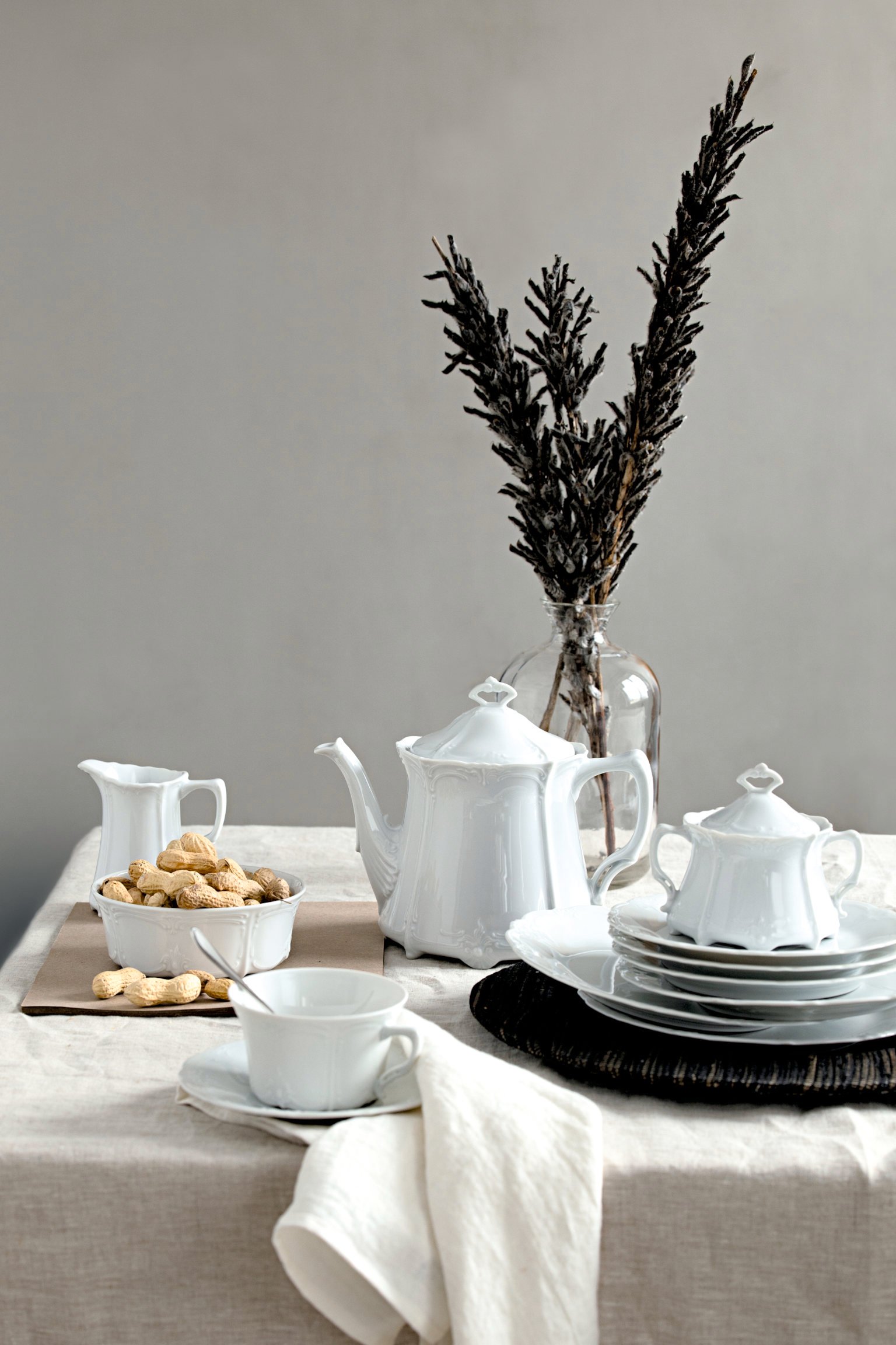 Baronesse white tea pot, tea cup, sugar bowl, milk jug arranged on table with linen cloth with large branches in a glass vase