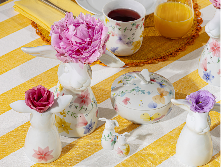 Colourful Hutschenreuther tableware with a delicate floral pattern on a yellow and white striped tablecloth, arranged with a vase, sugar bowl, cup and fresh flowers.