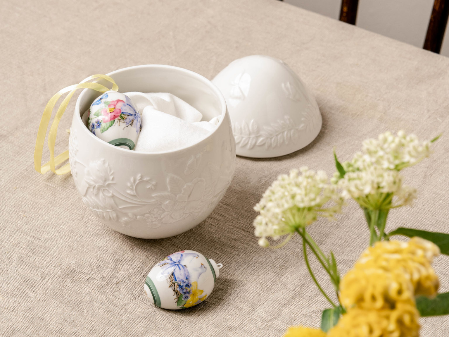 Hutschenreuther Maxi Dose aus Porzellan in Ei-Form mit Porzellan-Eier-Anhängern und Blumen im Vordergrund