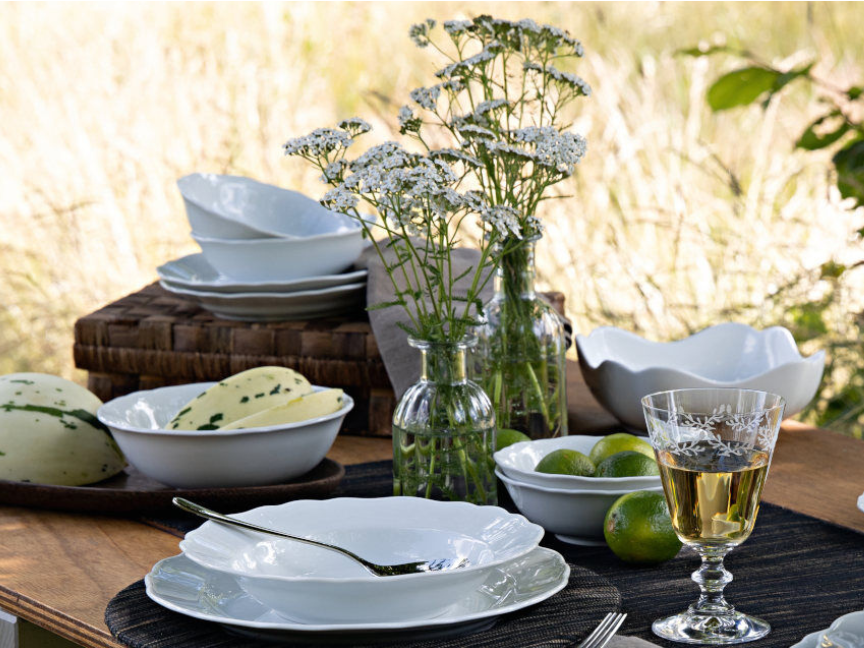 Dettaglio di una tavola estiva con porcellane bianche, meloni e fiori di campo