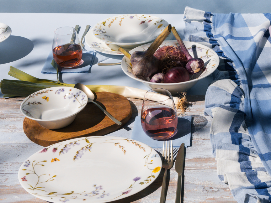 Spring table setting with floral Rosenthal dinnerware, rosé wine, and fresh ingredients – elegantly styled outdoors.