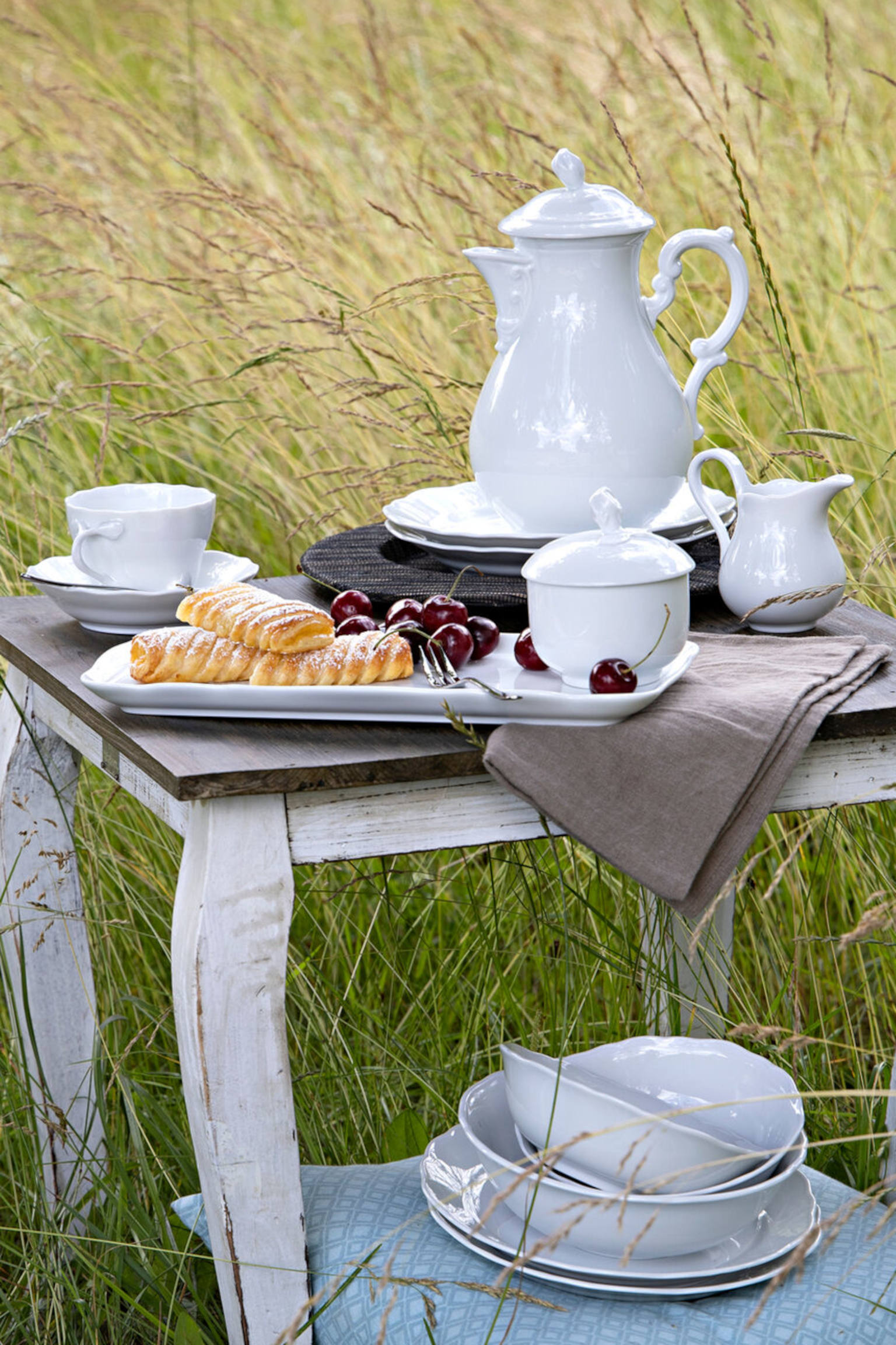 White dining collection Maria Theresia tea pot, sugar bowl, milk jug, tea cup on a wooden table in a summer meadow