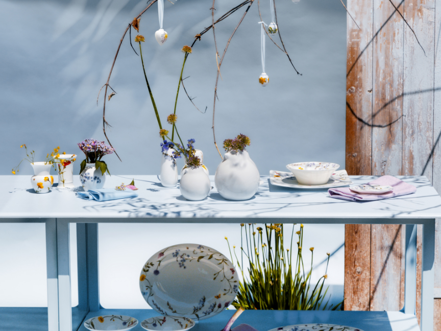 Hutschenreuther tableware with floral patterns on a decorated outdoor table shelf, with plates, bowls, vases and spring branches in a stylish arrangement.